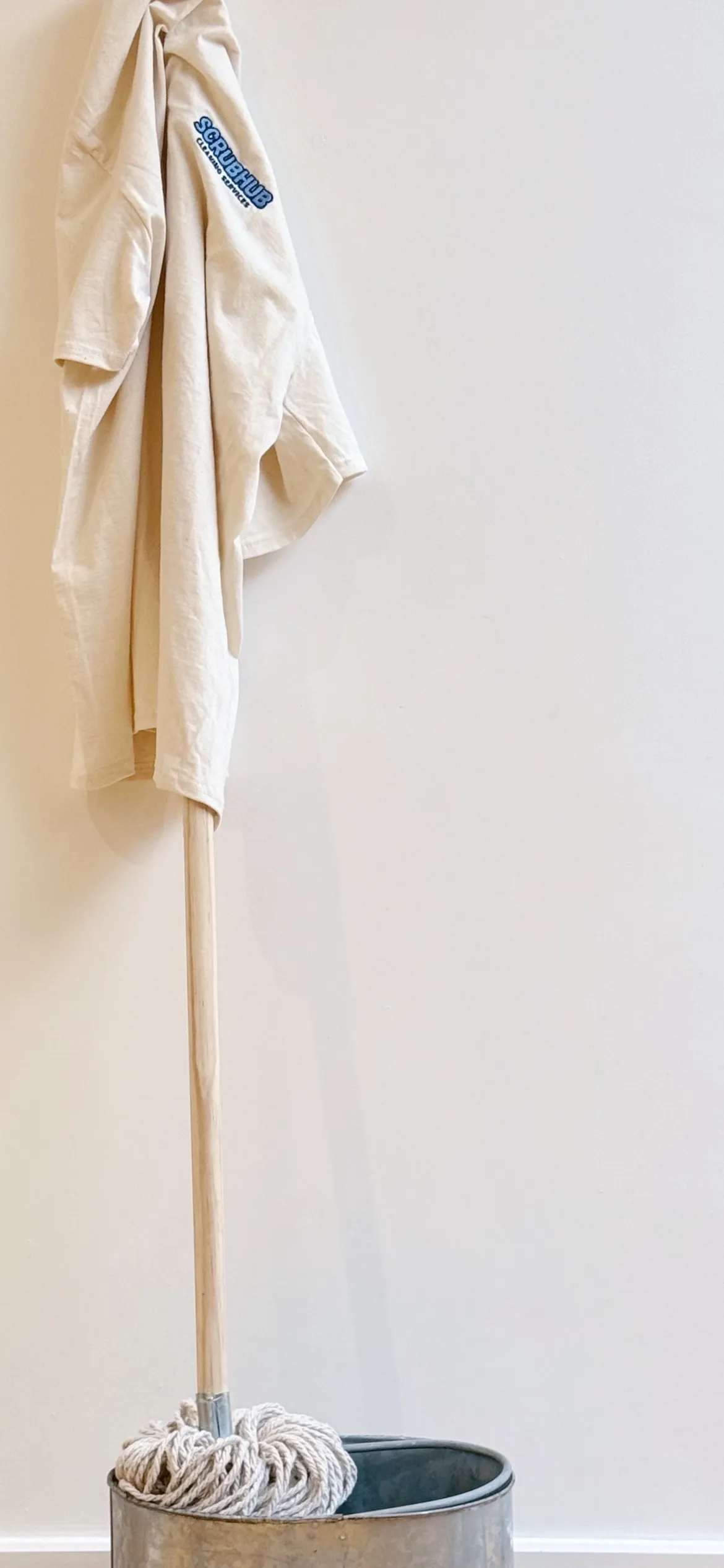 A Scrubhub Cleaning Services branded t-shirt hanging on a mop in a galvanised bucket